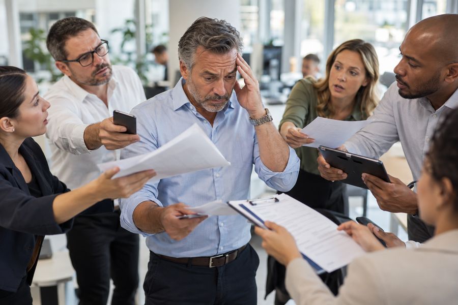 Empresário no meio do escritório, cercado de pessoas estendendo papéis e telefones